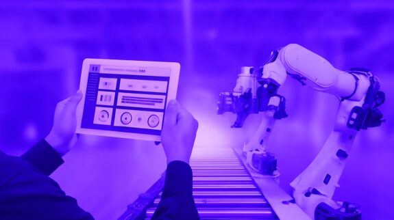 Giải Pháp Tự Động Hóa Nhà Máy Kỹ sư sử dụng máy tính bảng để điều khiển cánh tay robot công nghiệp trên dây chuyền sản xuất tự động.